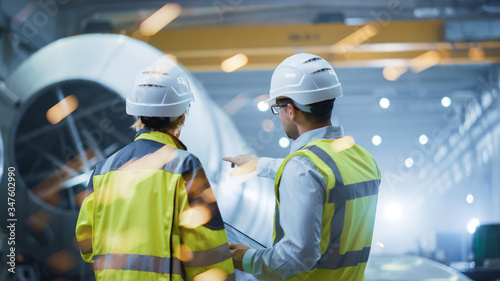 Fotografía Two Heavy Industry Engineers Stand in Pipe Manufacturing Factory, Use Digital Tablet Computer, Have Discussion