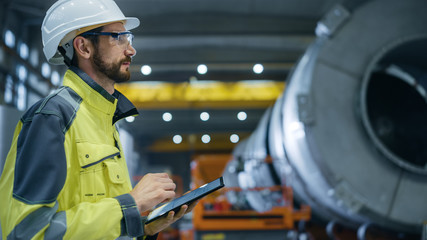 Wall Mural - Heavy Industry Engineer in Pipe Manufacturing Factory, Use Digital Tablet Computer. Facility for Construction of Oil, Gas and Fuel Pipeline Transportation Products. Side View