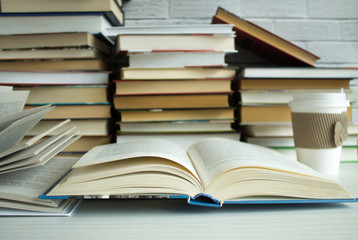 Clutter on the table - a lot of open and closed books close-up and a paper Cup of coffee with a lid