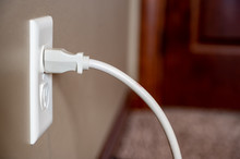 Side View Of White Power Cord Plugged Into A White Wall Outlet