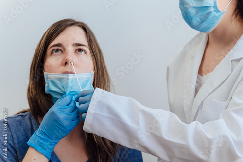 Female doctor in a protective suit taking a nasal swab from a person to test for possible coronavirus infection. Nasal mucus testing for viral infections. Medical Concept. Covid