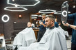 © Svitlana - Look here. Two barbers holding mirrors and showing haircuts to father and son sitting in armchair at modern barbershop. Family visiting barber shop