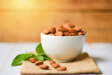 Wall Mural - Almonds nuts on bowl with leaf almonds on wooden background - Roasted almond for snack