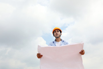 Asian man malay worker engineer management hard safety hat helmet at construction site reading seeing plan blue sky