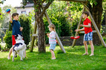 Wall Mural - Two kids boys and little toddler girl playing with family dog in garden. Three children, adorable siblings having fun with dog. Happy family outdoors. Friendship between animal and kids