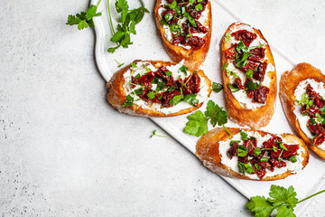 Wall Mural - Toasts with sun-dried tomatoes and cream cheese on white board, white background, top view.