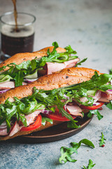 Canvas Print - Two fresh baguette sandwiches with meat, tomato, cucumber and arugula on gray background.