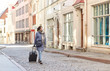 © Syda Productions - health, safety and pandemic concept - young woman in protective face mask with travel bag walking along empty street of old town in tallinn city