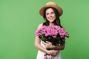 Image of cheerful pretty woman in straw hat smiling and holding flowers