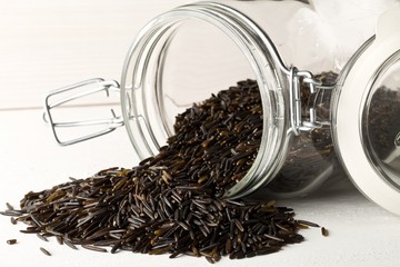 Wall Mural - Heap of uncooked, raw, black wild rice grains in glass storage jar on white table background