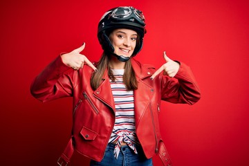 Wall Mural - Young beautiful brunette motocyclist woman wearing motorcycle helmet and red jacket looking confident with smile on face, pointing oneself with fingers proud and happy.