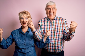 Wall Mural - Senior beautiful couple standing together over isolated pink background celebrating surprised and amazed for success with arms raised and open eyes. Winner concept.