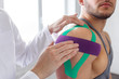 © YURII MASLAK - Kinesiology taping. Physical therapist applying kinesiology tape to patient shoulder. Female therapist treating injured shoulder of male athlete. Post traumatic rehabilitation, sport physical therapy.