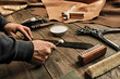 Working process of the leather belt in the leather workshop. Man holding tool. Tanner in old tannery. Wooden table background. Close up man arm. Maintenance concept. Goods production.