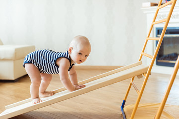 cute baby performs gymnastic exercises on a wooden home sports complex stairs and rings. children's 