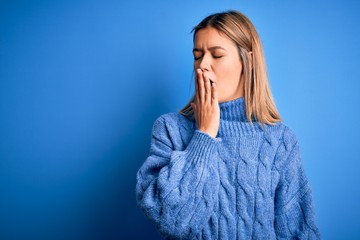 Sticker - Young beautiful blonde woman wearing winter wool sweater over blue isolated background bored yawning tired covering mouth with hand. Restless and sleepiness.