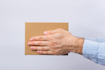 Wall Mural - Square cardboard box in male hands. Delivery of parcels. Side view.