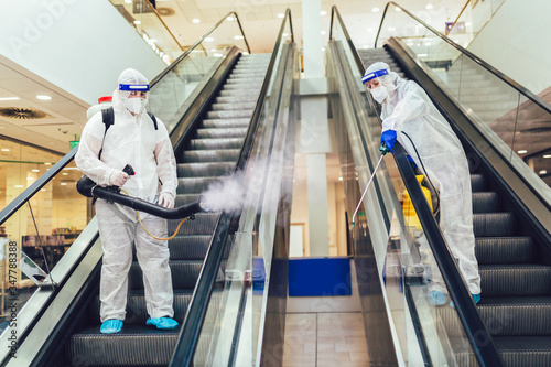 Fotografía Professional workers in hazmat suits disinfecting indoor of mall, pandemic healt