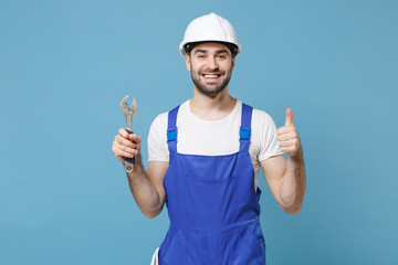 Smiling man in coveralls protective helmet hardhat hold adjustable wrench isolated on blue background. Instruments accessories for renovation apartment room. Repair home concept. Showing thumb up.