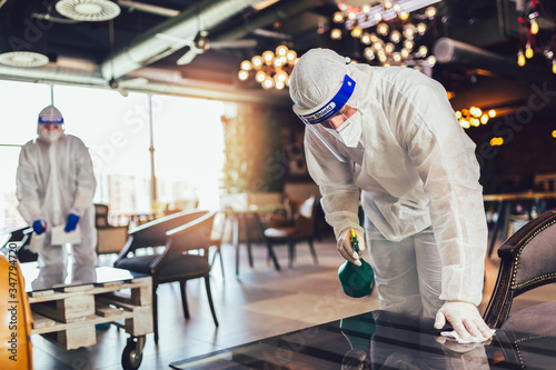 Fotografía Professional workers in hazmat suits disinfecting indoor of cafe or restaurant,