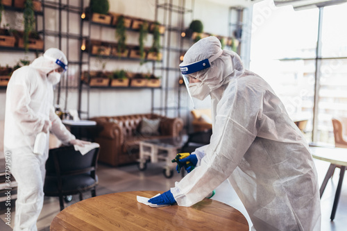 Fotomural Professional workers in hazmat suits disinfecting indoor of cafe or restaurant,