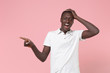 © ViDi Studio - Excited young african american man guy in white polo shirt posing isolated on pastel pink wall background. People lifestyle concept. Mock up copy space. Pointing index finger aside, put hand on head.