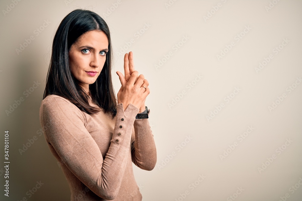 Young brunette woman with blue eyes wearing casual sweater over isolated white background Holding symbolic gun with hand gesture, playing killing shooting weapons, angry face