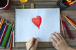 © aldarinho - Flat lay of hands drawing a heart with colored pencils on white paper. Art studio workplace concept