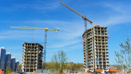 Construction site with two cranes against the classic blue sky.