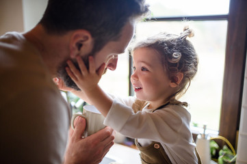 Father giving drink to sick toddler daughter indoors at home.