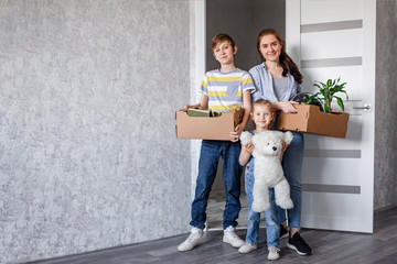 The family moves into a new apartment, a little girl runs in the door, holding cardboard boxes in the background. Mother with her son and daughter move things to a new home.