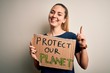 © Krakenimages.com - Young beautiful blonde woman with blue eyes asking for protect planet holding banner surprised with an idea or question pointing finger with happy face, number one