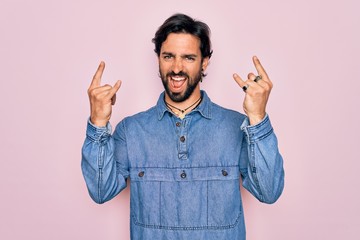 Wall Mural - Young handsome hispanic bohemian man wearing hippie style over pink background shouting with crazy expression doing rock symbol with hands up. Music star. Heavy concept.