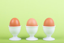 Three Brown Eggs In White Eggs Cups Before Green Background