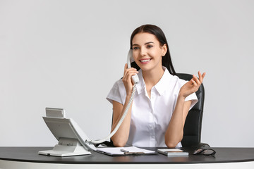 Wall Mural - Beautiful young secretary talking by telephone at table on white background