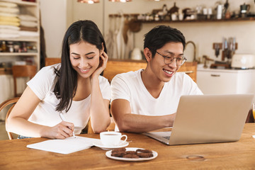 Poster - Image of multicultural couple making notes in planner and using laptop