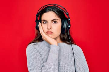 Sticker - Young beautiful girl wearing modern headphones listening to music over red background thinking looking tired and bored with depression problems with crossed arms.