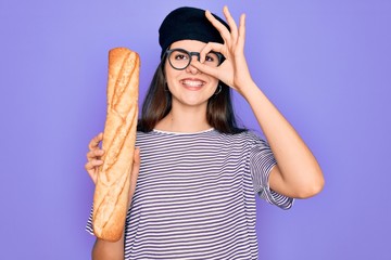 Sticker - Young beautiful girl wearing fashion french beret holding fresh baked bread baguette with happy face smiling doing ok sign with hand on eye looking through fingers