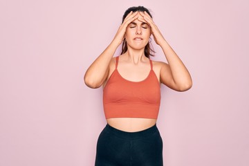 Sticker - Young beautiful fitness woman wearing sport excersie clothes over pink background suffering from headache desperate and stressed because pain and migraine. Hands on head.