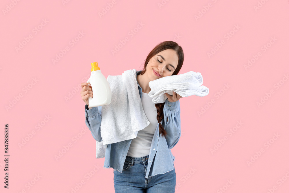 Beautiful young woman with laundry and detergent on color background