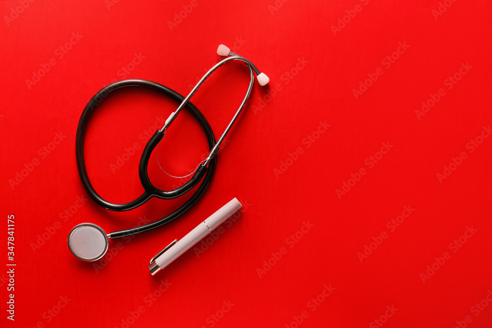 Modern flashlight with stethoscope on color background