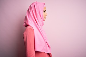 Canvas Print - Young beautiful girl wearing muslim hijab standing over isolated pink background looking to side, relax profile pose with natural face and confident smile.