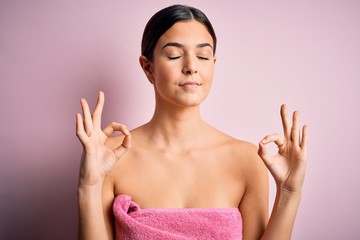 Poster - Young beautiful girl wearing towel shower after bath standing over isolated pink background relax and smiling with eyes closed doing meditation gesture with fingers. Yoga concept.