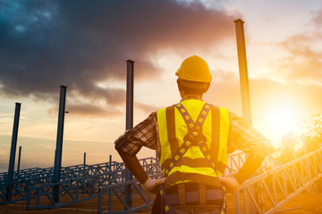 The construction engineer supervises the construction site and the sunset background