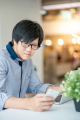 Wall Mural - Smart Asian businessman in casual clothing using smartphone and laptop computer working at home office. Male manager using mobile app for social media and online news. Technology for business strategy