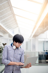Asian man entrepreneur wearing glasses and headphones using laptop at home office. Businessman working with personal computer thinking about business project. Work smart with modern technology.