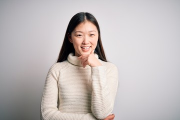 Sticker - Young beautiful asian woman wearing casual sweater standing over isolated background looking confident at the camera smiling with crossed arms and hand raised on chin. Thinking positive.