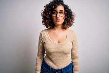 Wall Mural - Young beautiful curly arab woman wearing casual t-shirt and glasses over white background Relaxed with serious expression on face. Simple and natural looking at the camera.