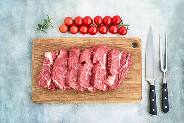 Fresh raw beef steaks with pepper and tomatoes on wooden cutting board board. Copy space, top view.