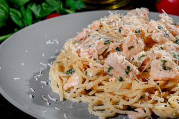 Wall Mural - Delicious Italian spaghetti pasta with salmon, fresh basil leaves and grated parmesan cheese on dark background